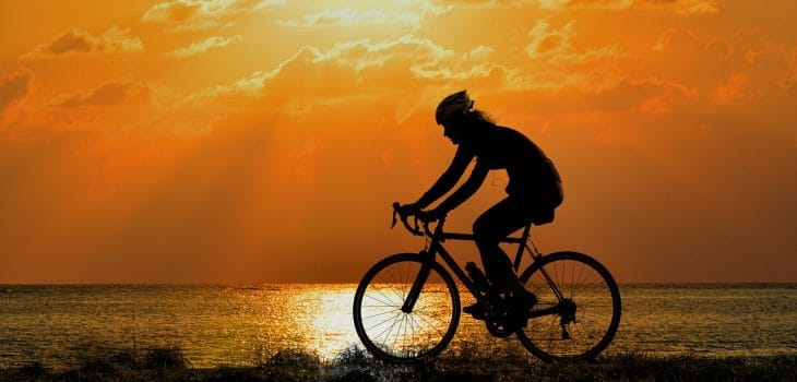 Silhouette d'une cycliste féminine roulant sur un vélo gravel au coucher de soleil avec un fond marin lumineux.