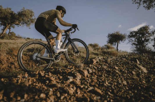 Gravel Van Rysel GCR Force AXS XPLR posé sur un chemin en pleine nature, vue latérale du vélo en carbone noir mat.